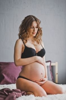 Happy pregnant girl in black underwear stroking big belly with baby.. Portrait of a pregnant woman in her underwear 1281.