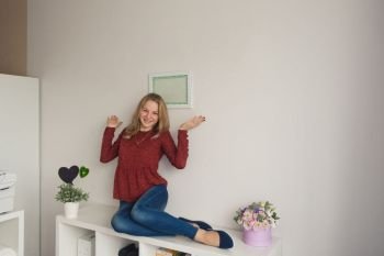 Girl sitting on a book shelf in the white wall.. The girl pointing at the writing on the wall 9068.