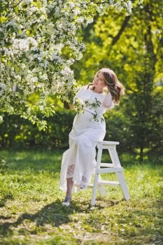 The girl in the position dressed in white resting in a beautiful garden.. A pregnant woman walks in the flowered gardens 8229.