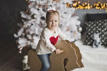 Portrait of a baby on a paper horse on the Christmas tree.. Little girl riding a toy horse 7081.