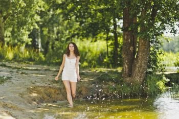 Portrait of girl walking on the water of the lake.. Girl in a white short dress, walks along the waters edge of the pond 6333.