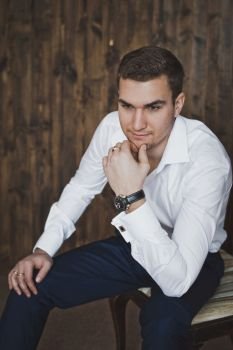 Portrait of a man in the background of a wooden wall.. Portrait of a young man sitting on a chair 6392.