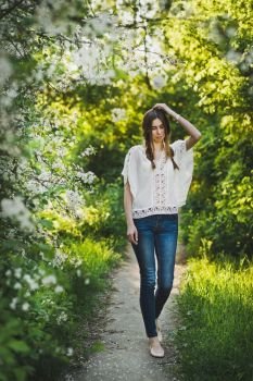 Girl in white blouse walking through the garden.. The girl goes on a footpath among a blooming garden 6101.