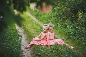 Children sit in the garden on a rustic path.. The girls in pink dresses sitting between rural paths 6628.
