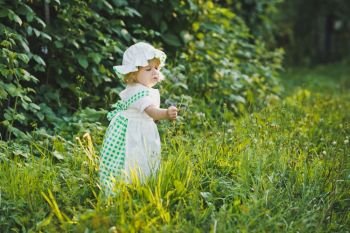 A child in a dress with apron and bonnet on.. A child walks in the summer garden 4645.