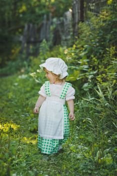 Little girl in green and white dress walking in the garden.. Girl in a dress in green peas in the garden 4656.