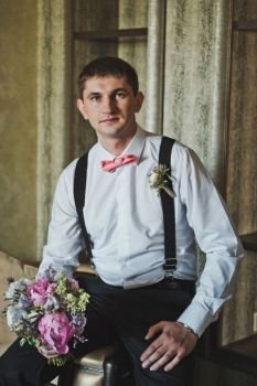 Portrait of a young man sitting on a chair in the room.. The bridegroom waiting for the wedding 3718.