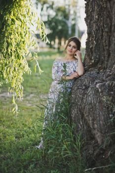 Portrait of a girl at the trunk of a weeping willow.. A beautiful portrait of a pregnant girl near a drooping branch of a weepin