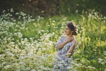 Simple female beauty on a glade of flowers of the kupyr forest.. Portrait of a happy pregnant woman in a clearing of white flowers of a for