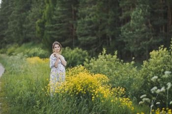 Beautiful girl in a long light dress in a clearing with yellow flowers.. The beauty of the female figure in a forest glade of yellow flowers 1702.