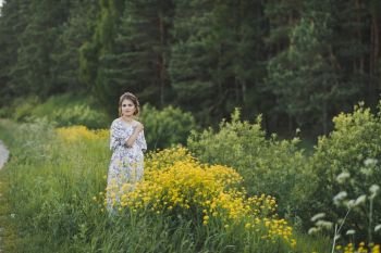 Beautiful girl in a long light dress in a clearing with yellow flowers.. The beauty of the female figure in a forest glade of yellow flowers 1703.