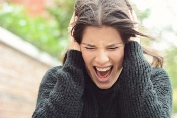 Angry furious woman screaming with rage against brick wall
 