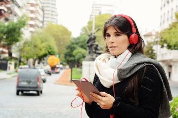 Portrait of young beautiful woman with red headphones listening music. Outdoors. Urban concept.