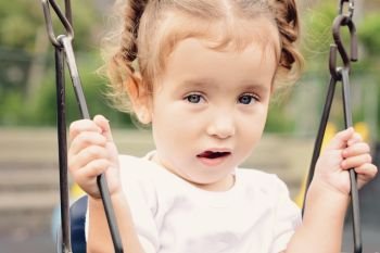 Cute little girl on a swing in the park. Summer portrait