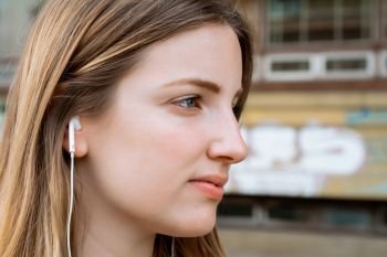 Portrait of young blond woman listening to music with Earphones. Outdoors