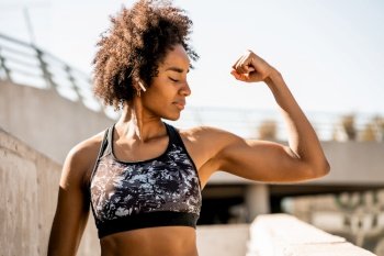 Portrait of afro athlete woman flexing and showing muscles while standing outdoors. Sport and healthy lifestyle.. Afro athlete woman flexing and showing muscles.