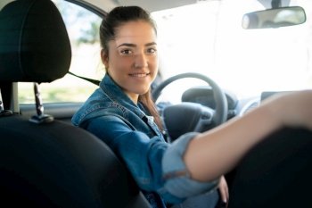 Portrait of young woman driving her car and looking at back seat to camera. Transport concept.. Woman driving her car and looking at back seat