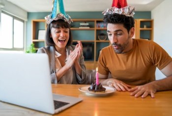 Portrait of a couple celebrating birthday on a video call with a laptop from home. Couple celebrating birthday online in quarantine time. New normal lifestyle concept.. Couple celebrating birthday on a video call at home.