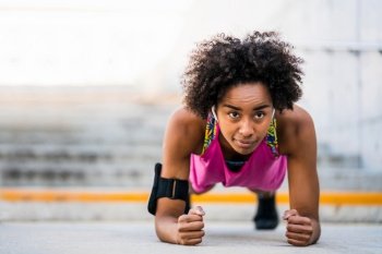 Portrait of afro athlete woman doing pushups on floor outdoors. Sport and healthy lifestyle concept.