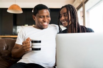 Portrait of young couple spending time together and using laptop while sitting on couch at home. New normal lifestyle concept.