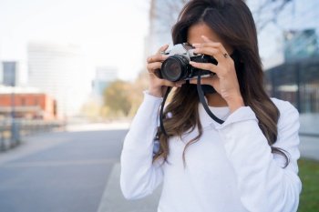 Portrait of young woman using a professional digital camera while standing outdoors on the street. Photography concept