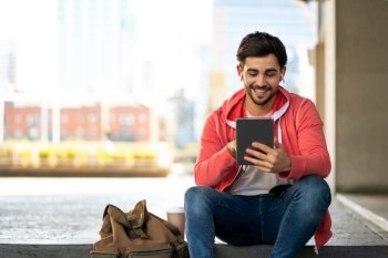Portrait of young man using digital tablet while sitting outdoors. Urban concept.