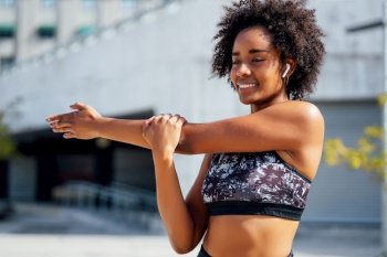 Afro athletic woman stretching her arms and warming up before exercise outdoors. Sport and healthy lifestyle.