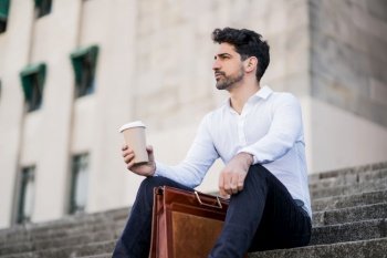 Portrait of a business man drinking a cup of coffee on a break from work while sitting on stairs outdoors. Business concept.