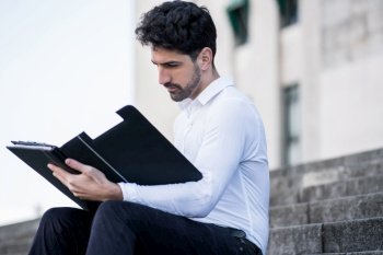 Portrait of young business man reading files while sitting on stairs outdoors. Business and success concept.