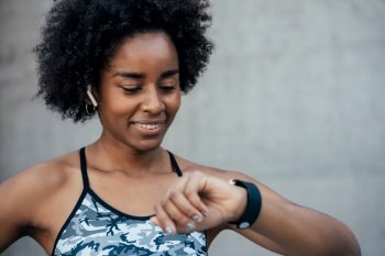Afro athletic woman checking time on her smart watch while work out outdoors. Sport and healthy lifestyle concept.