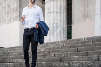 Businessman holding a cup of coffee on his way to work outdoors. Business concept.