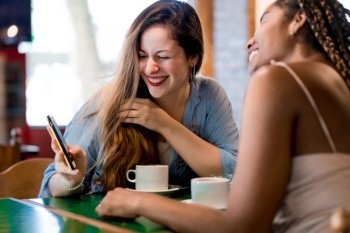 Two female friends using a mobile phone while drinking a cup of coffee at a coffee shop. Friends concept.
