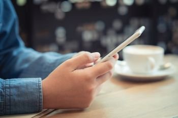 Hand of asian woman using smartphone on wooden table in coffee shop