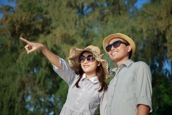 Asian couples are pointing their fingers at the beach at summer time, Men and women wearing sunglasses are smiling and looking at the sea.