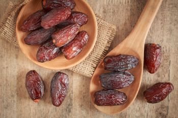 close up picture of dates palm fruit in cup and spoon on wooden table background. Dates palm fruit dry is snack healthy.