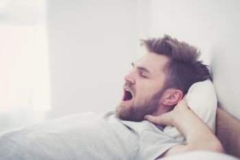 Handsome young american male yawn sleeping in bed at home - healthcare concept.