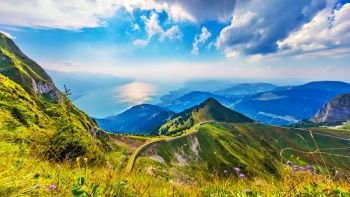 Scenic summer panorama from Rochers de Naye mountain peak with green grassy hills, flower meadows and Geneva Lake in Alps, Switzerland