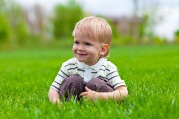 Smiling little boy sitting in fresh grass. Shallow DOF effect
