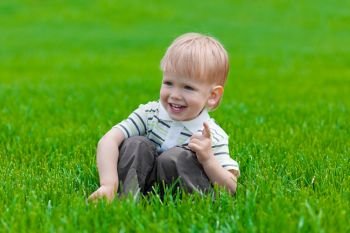 Little boy sitting and dreaming in green grass. Shallow DOF effect