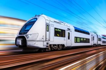 Railroad travel and railway tourism transportation industrial concept: scenic summer view of modern high speed passenger commuter train on tracks with motion blur effect