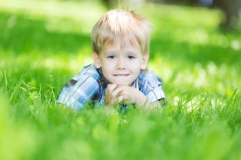 Portrait of a little boy laying on the fresh grass loan in the city park in summer