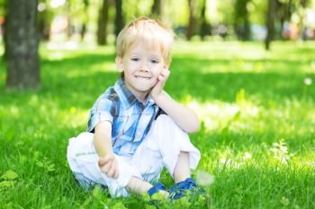 Portrait of a little boy sitting on the fresh grass loan in the city park in summer