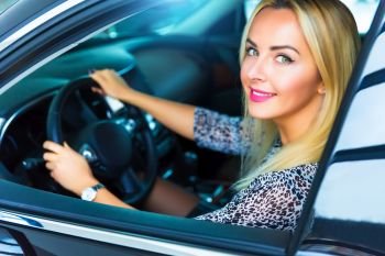 Happy smiling young blond woman in the modern luxury car