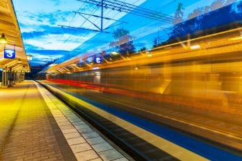 Railroad travel and transportation industry business concept: summer evening view of high speed commuter passenger train departing from railway station platform with motion blur effect