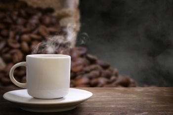 white coffee cup and coffee beans in hemp sack with steam on the wooden shelf or hot drink in mug isolated on black background