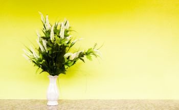 artificial flower in vase on yellow concrete wall background