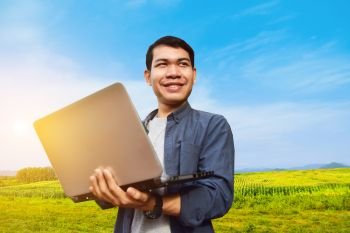 Asian man holding computer notebook montage on blue sky and farm background ,smart farmer technology