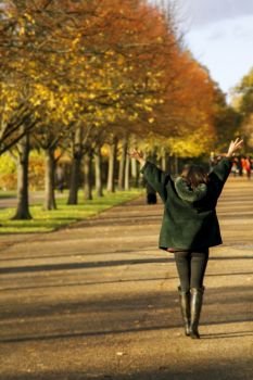 Young Asian woman happy in autumn park with open arms in the hair. Shot from behind