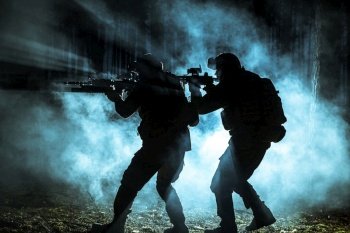 Black silhouettes of pair of soldiers in the smoke moving in battle operation. Back light. Black silhouettes of soldiers