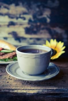 grey cup of tea on a wooden table against the background of a baguette and sunflower